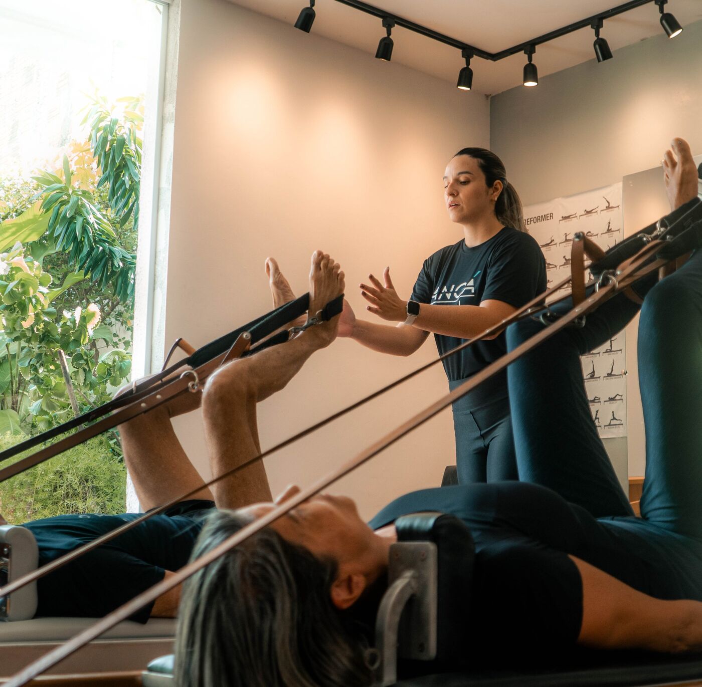 Instrutora guiando uma aula no Reformer, na sala com janela para o jardim