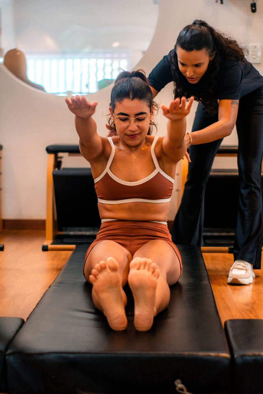 Instrutora guiando de perto os braços de uma aluna durante o exercício