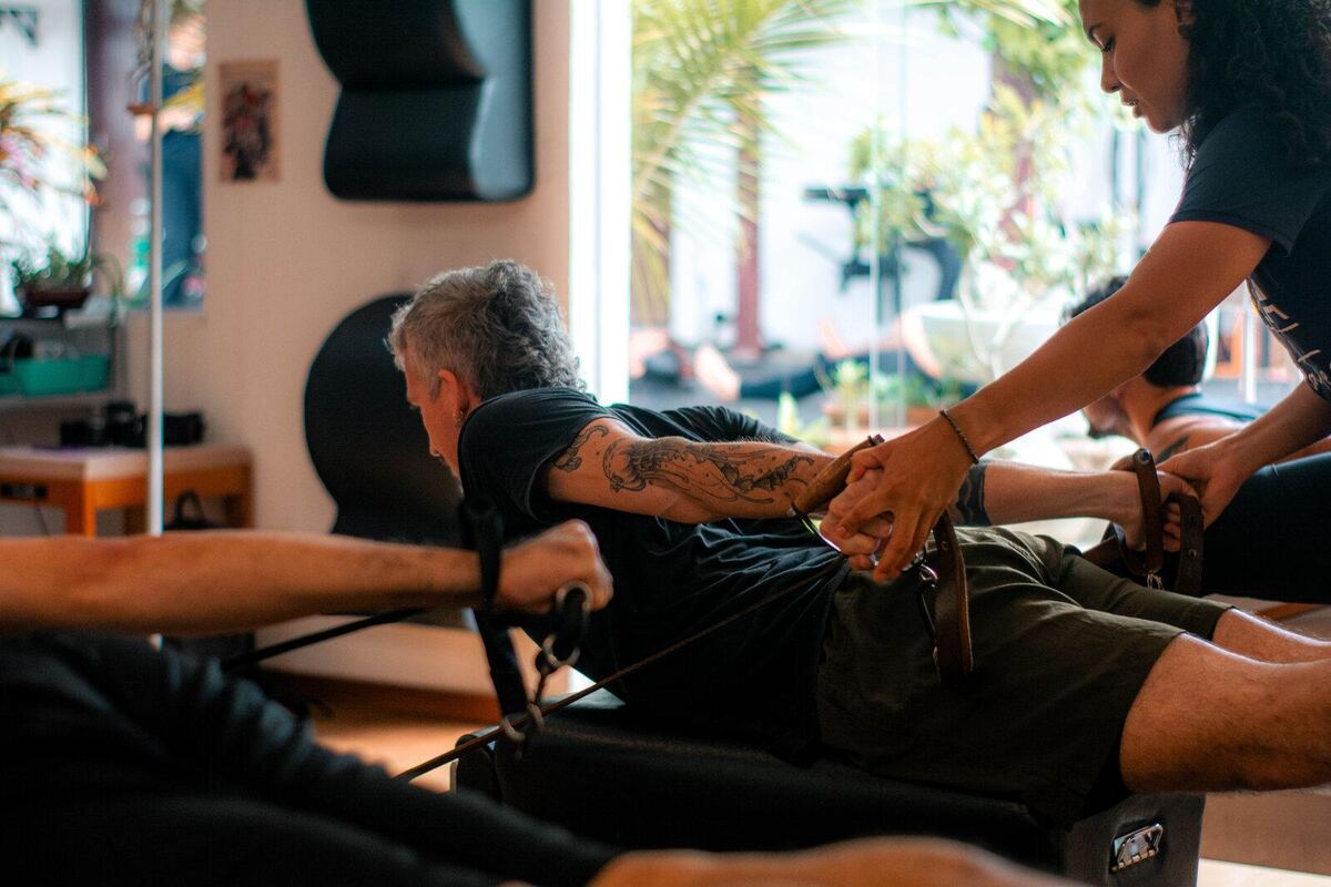 Instrutora ajustando com as mãos o movimento de um aluno no Reformer